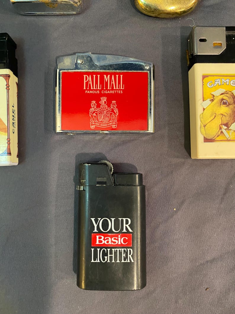 May include: A collection of lighters, including a black lighter with the text "YOUR Basic LIGHTER", a red lighter with the text "PALL MALL FAMOUS CIGARETTES", and a white lighter with the text "GAME" and a camel illustration.
