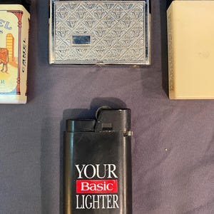 May include: Three lighters, one with a silver finish and a patterned design, one with a black finish and the text "YOUR Basic LIGHTER", and one with a gold finish and a camel logo.