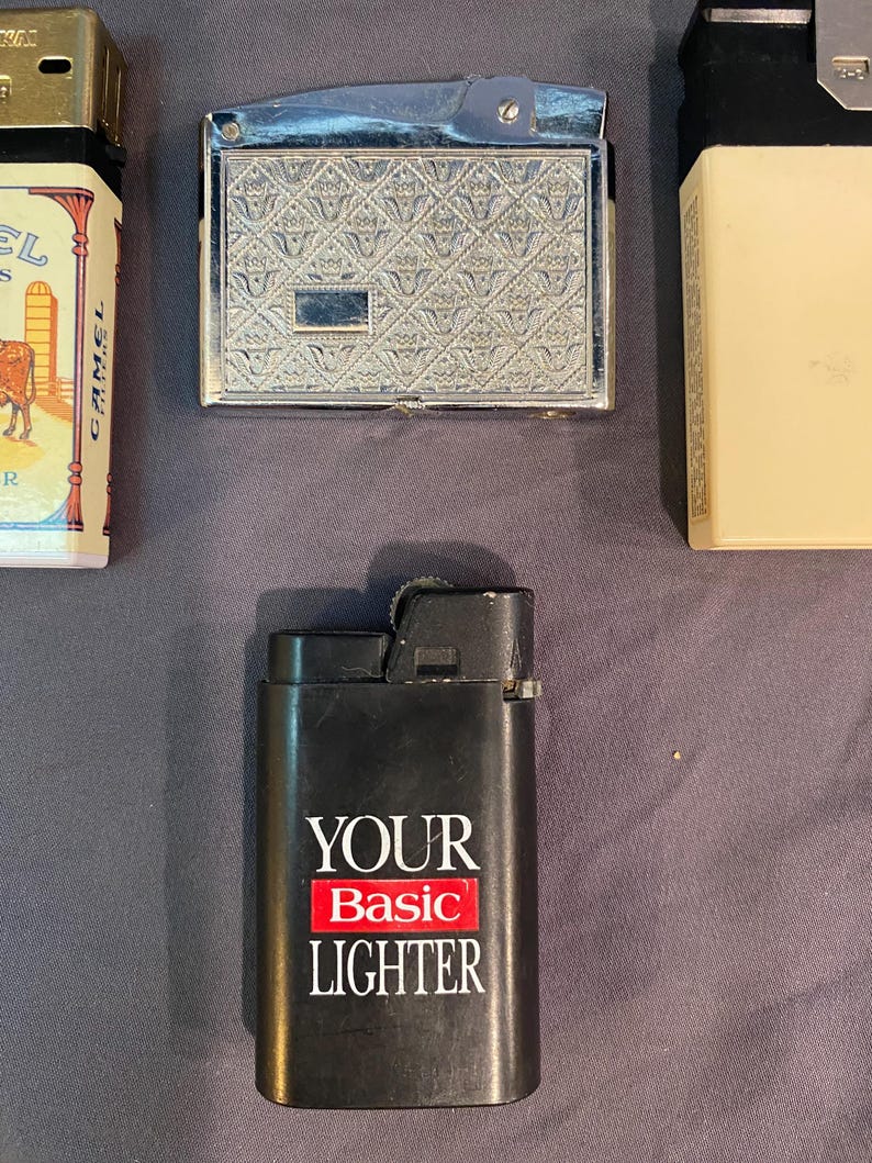 May include: Three lighters, one with a silver finish and a patterned design, one with a black finish and the text "YOUR Basic LIGHTER", and one with a gold finish and a camel logo.
