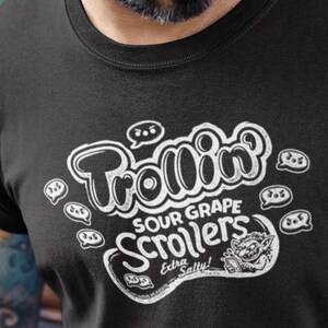 May include: Black t-shirt with a white graphic that reads "Trollin Sour Grape Scrollers Extra Salty!" The design includes speech bubbles and a cartoon troll. The shirt has rolled-up sleeves.
