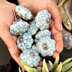 Könnte beinhalten: Eine Sammlung von blauen und weißen Keramik-Schrankknöpfen mit floralem Muster. Die Knöpfe haben eine silberne Metallbasis und sind perfekt, um jedem Raum einen Hauch von Landhausstil zu verleihen.