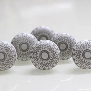 Op de afbeelding: Zes witte keramische ladegrepen met een grijs mandala-ontwerp.