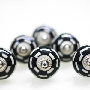 Peut inclure: Six boutons de porte en céramique noire et blanche avec un centre argenté. Les boutons ont un motif géométrique.