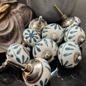 Könnte beinhalten: Eine Sammlung von acht Keramik-Schrankknöpfen mit weißer Basis und blauem Blumenmuster. Die Knöpfe haben eine silberne Metallbasis und eine Schraube.