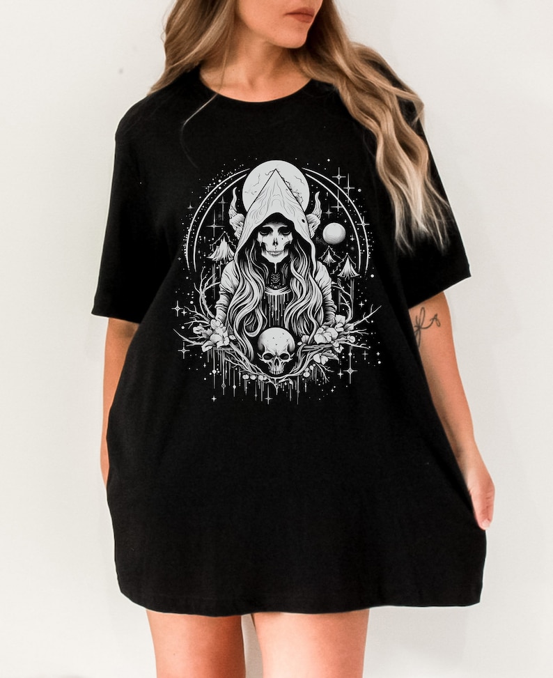 May include: Black oversized t-shirt featuring a white graphic print of a hooded figure with horns, a skull, and a crescent moon.