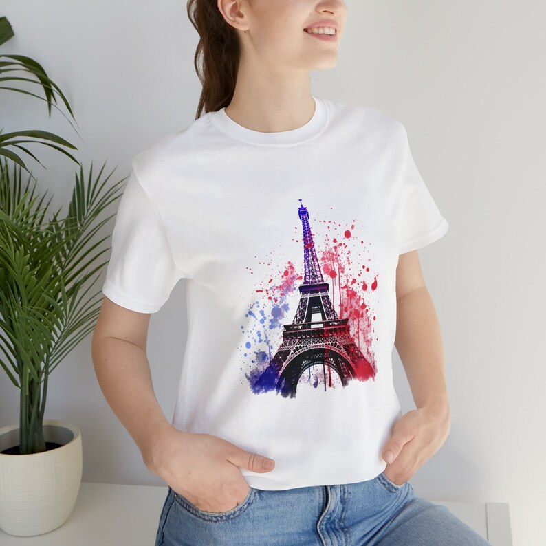 Op de afbeelding: Wit T-shirt met een aquarel afbeelding van de Eiffeltoren in tinten blauw, rood en paars.