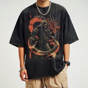 K&ouml;nnte beinhalten: Schwarzes T-Shirt mit einem Grafikdruck eines Samurai-Kriegers, der gegen einen roten Drachen k&auml;mpft. Der Drache ist um den Samurai gewickelt, und das Design ist vor einem schwarzen Hintergrund platziert. Das Shirt hat einen Used-Look.