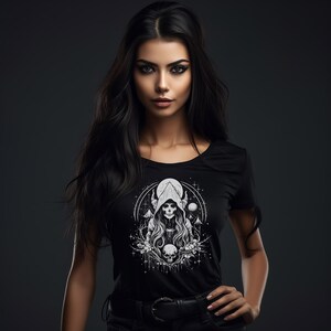 May include: A woman with long black hair is wearing a black t-shirt with a white graphic print of a hooded figure with a skull face. The graphic also includes a crescent moon, stars, and a skull.
