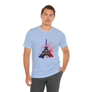 Op de afbeelding: Een lichtblauw t-shirt met een aquarel afbeelding van de Eiffeltoren in tinten rood en blauw.
