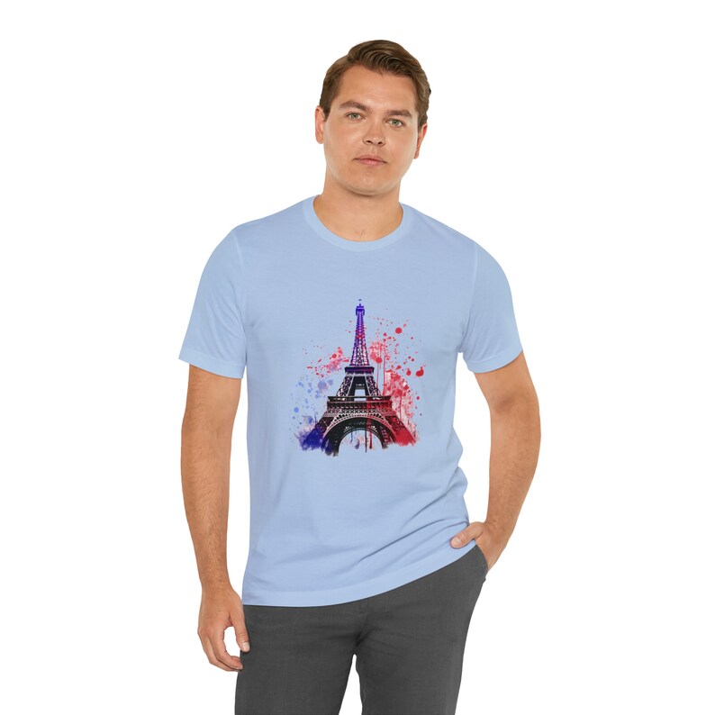 Op de afbeelding: Een lichtblauw t-shirt met een aquarel afbeelding van de Eiffeltoren in tinten rood en blauw.