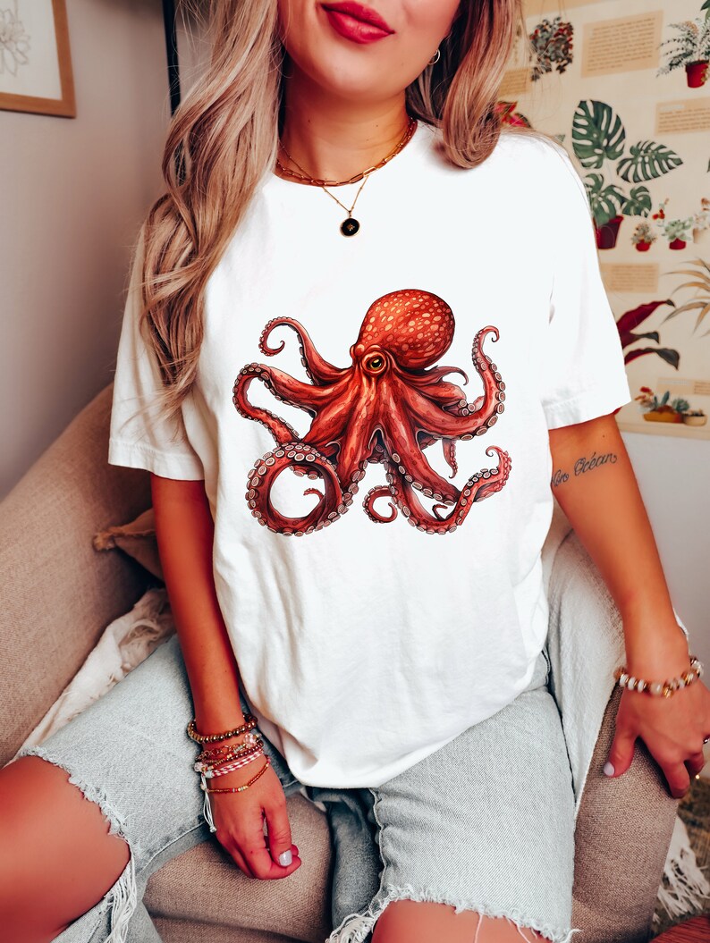 May include: White t-shirt with a red octopus graphic. The octopus has eight tentacles and a large eye. The shirt is being worn by a person.