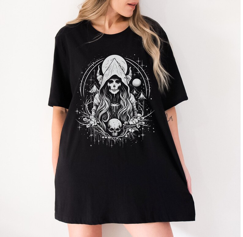 May include: Black t-shirt featuring a white graphic of a hooded figure with horns, a skull, and a moon in a woodland setting.
