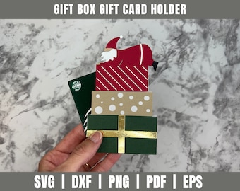 Puede incluir: Una caja de regalo roja y blanca a rayas con una figura de Papá Noel en la parte superior. La caja de regalo está apilada sobre otras dos cajas de regalo, una con lunares marrones y blancos y la otra con rayas verdes y doradas. Las cajas de regalo se sostienen en una mano.