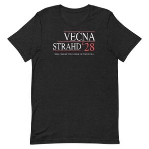 Könnte beinhalten: Ein anthrazitfarbenes Kurzarm-T-Shirt mit weißem und rotem Text, der VECNA STRAHD '28 und den Satz WHY CHOOSE THE LESSER OF TWO EVILS lautet. Das T-Shirt hat einen Rundhalsausschnitt und eine melierte Stoffstruktur auf dem gesamten Kleidungsstück.