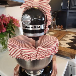 May include: A black KitchenAid stand mixer with a red and white striped fabric cover and a red and white striped bow on top.