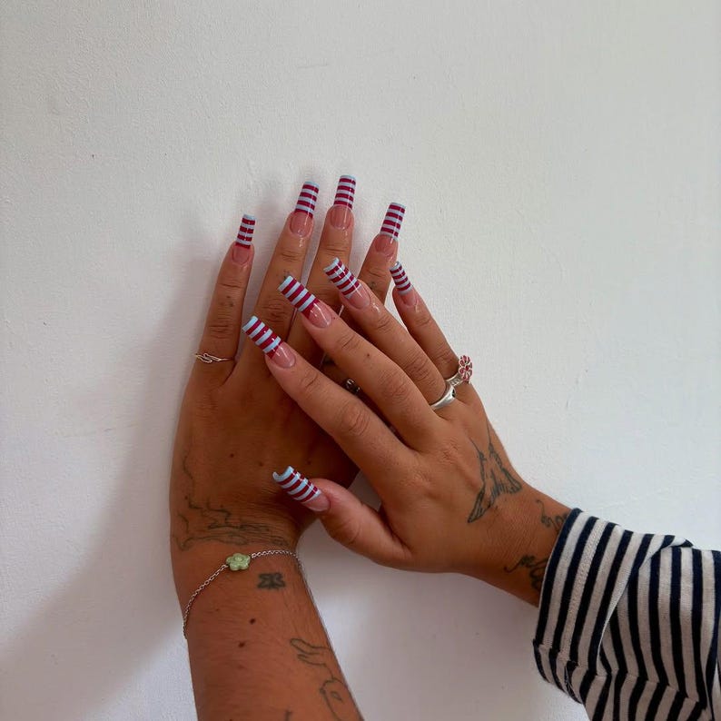 May include: Long, square-shaped acrylic nails with a clear base and a striped design in burgundy and light blue. The nails are adorned with a series of thin, horizontal stripes. The design is repeated on each nail, creating a cohesive look.