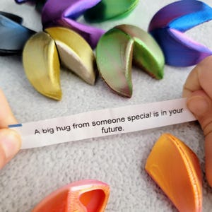 May include: A variety of colorful fortune cookies with a white paper fortune that reads "A big hug from someone special is in your future."