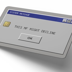 May include: A rectangular credit card with a grey surface and a gold EMV chip. The card features a digital interface design resembling a computer system message window with a blue header, the text THIS MF MIGHT DECLINE, and an OK button.