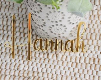 Può includere: Carta di nome con glitter dorati con il nome "Hannah" scritto in corsivo.