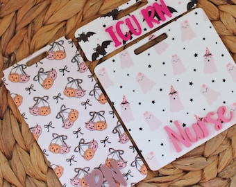 May include: Three Halloween-themed badge holders with pink accents. One features pumpkins, another ghosts, and the third bats. The words "ICU RN" and "Nurse" are displayed in pink. The background is a woven texture.