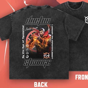 May include: Two charcoal gray t-shirts. The back of one shirt features a graphic of a character with the text "doctor strange" and "Stephen Strange". The front of the other shirt has a white symbol. The text "By the Eye of Agomatto!" is also visible.