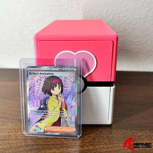 May include: A pink and white card storage box with a heart design, next to a card in a protective sleeve. The card features the text "Erika's Invitation" and a character illustration. The box has a rounded design.