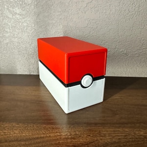 May include: A red and white storage box with a black stripe and a white button. The top half is red, and the bottom half is white. The box is rectangular and sits on a wooden surface.