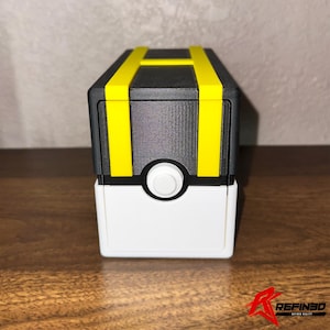 May include: A black and white box with yellow accents. The box has a white base, a black top with yellow stripes, and a white circular button. The design is reminiscent of a popular animated series.