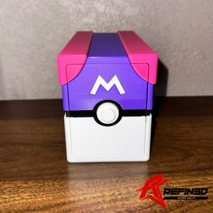 May include: A multi-colored, rectangular box with a white base, purple center, and pink top. The center features a white "M" and a black circle with a white button. The box is sitting on a wooden surface.
