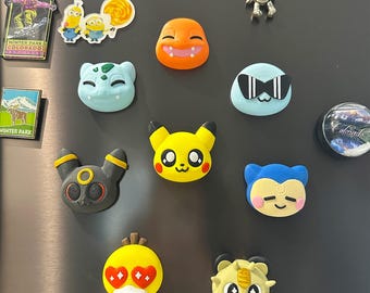 May include: A collection of colorful character magnets, including Pikachu, Charmander, and other cartoon figures. The magnets are in various shapes and sizes, with vibrant colors and detailed designs. Some magnets feature text, and the collection is displayed on a dark gray surface.