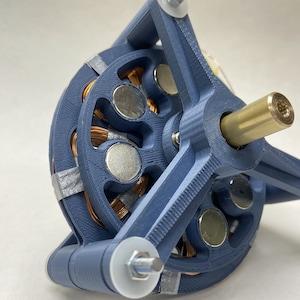 Könnte beinhalten: Nahaufnahme eines blauen 3D-gedruckten Motors mit Kupferdrahtwicklungen und Magneten. Der Motor hat eine Messingwelle und ist auf einem blauen 3D-gedruckten Sockel montiert.