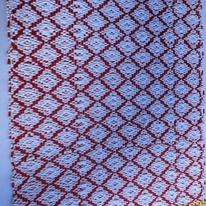Puede incluir: Una alfombra tejida roja y blanca con un patr&oacute;n de diamantes. El borde inferior de la alfombra es amarillo.