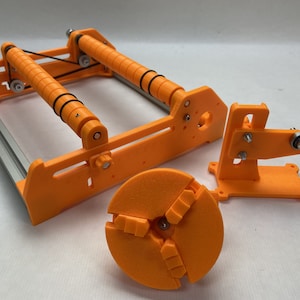 May include: A 3D printed orange filament winder with two spools, a tensioning knob, and a separate orange 3D printed chuck.