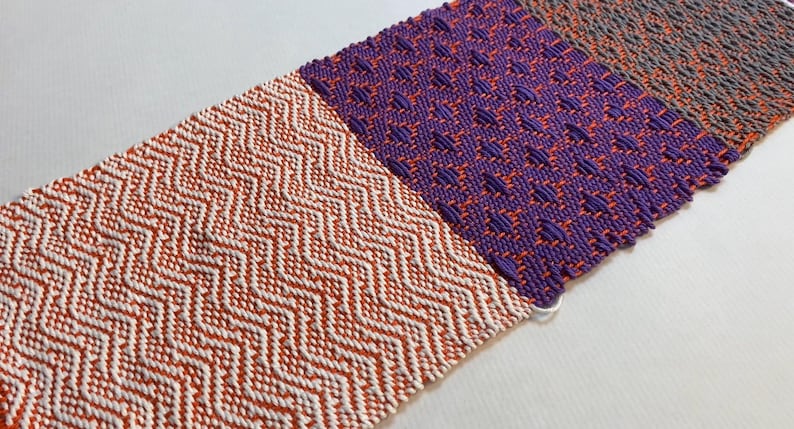 Puede incluir: Un tapiz tejido con cuatro patrones diferentes en naranja, blanco, morado y gris.