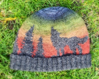 May include: A knitted hat with a colorful ombre design featuring a silhouette of a wolf and trees. The hat is gray with a dark gray brim.