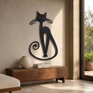 Puede incluir: Una pieza de arte mural de metal negro con forma de gato estilizado, cuerpo largo y esbelto, orejas puntiagudas y una cola prominente enroscada. El gato presenta bigotes alargados que se curvan hacia afuera a ambos lados de la cara.