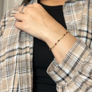 May include: A gold chain bracelet with small green and red gemstone beads.