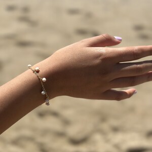 May include: A delicate gold chain bracelet with small white pearl accents. The bracelet is worn on a person's wrist.