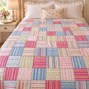 May include: A patchwork quilt featuring a repeating grid of square fabric blocks in alternating patterns and colors. The design includes light blue stripes, bright pink stripes, and soft sage green floral prints, all stitched together with visible quilting lines.