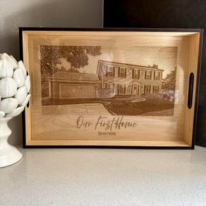 Puede incluir: Una bandeja de servir de madera con un borde negro y una imagen grabada con láser de una casa. El texto "Our First Home" y "Garcia Family" está grabado debajo de la imagen.
