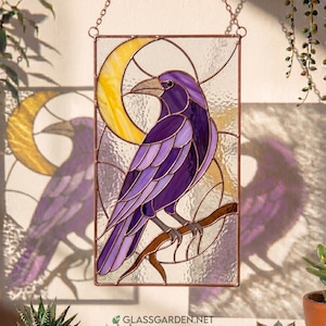 May include: A rectangular stained glass suncatcher featuring a purple raven perched on a brown branch against a yellow crescent moon. The piece is framed in copper metal with a chain for hanging and includes the text glassgarden.net at the bottom.