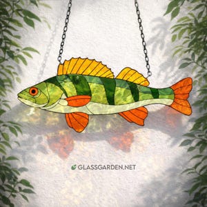Puede incluir: Decoración de pez de vidriera con aleta dorsal amarilla, aletas y cola naranjas y cuerpo verde y amarillo. El pez está suspendido por una cadena. La dirección del sitio web glassgarden.net es visible en la parte inferior.