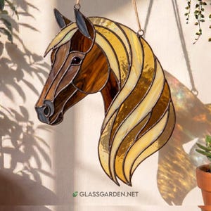 May include: Stained glass horse head with a flowing mane in shades of brown, amber, and gold. The artwork is suspended by a thin rope. The website address "glassgarden.net" is visible at the bottom.