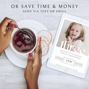Op de afbeelding: Een digitale tablet met een verjaardagsuitnodiging voor een kind dat drie jaar wordt. De uitnodiging bevat een foto van het kind, de tekst "three" en details over het feest, waaronder de datum, tijd en locatie. De tablet ligt op een wit houten oppervlak.