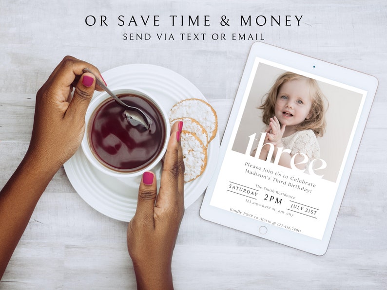 Op de afbeelding: Een digitale tablet met een verjaardagsuitnodiging voor een kind dat drie jaar wordt. De uitnodiging bevat een foto van het kind, de tekst "three" en details over het feest, waaronder de datum, tijd en locatie. De tablet ligt op een wit houten oppervlak.