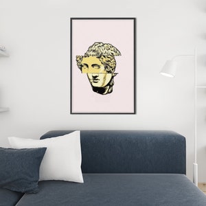 May include: A black framed print with a pink background featuring a yellow and black illustration of a broken statue of a woman's head.