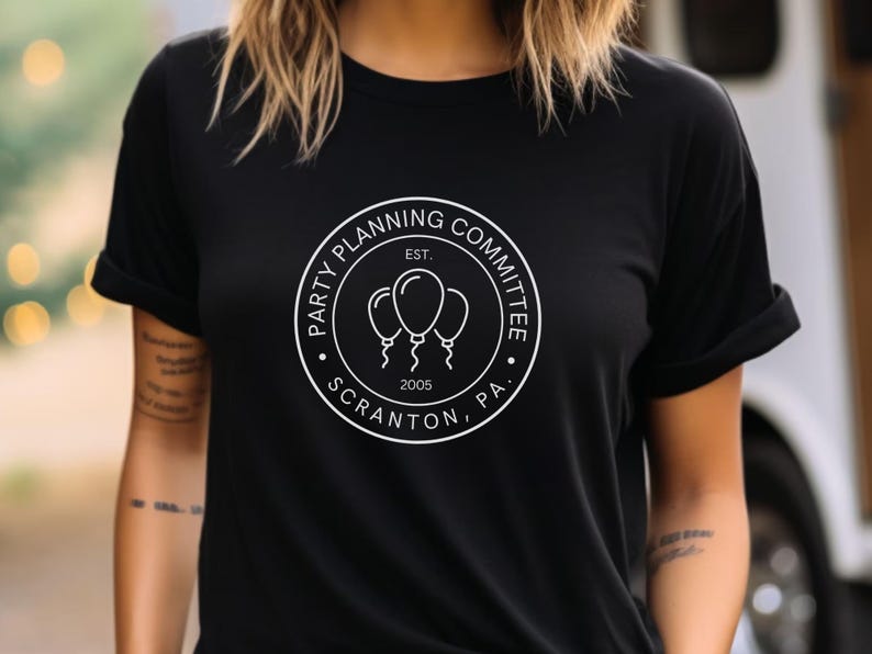 May include: Black t-shirt with a white circle graphic that says "Party Planning Committee" with a small image of three balloons and the text "Est. 2005 Scranton, PA."