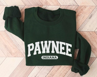Peut inclure: Un sweat-shirt vert foncé avec un texte blanc qui dit "PAWNEE INDIANA" dans une police d'écriture en arc.