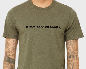 Könnte beinhalten: Olivgrünes T-Shirt mit dem schwarzen Text "FIST MY BUMP" und einer kleinen Grafik. Das kurzärmelige Oberteil hat einen Rundhalsausschnitt. Der Stoff scheint weich und meliert zu sein.