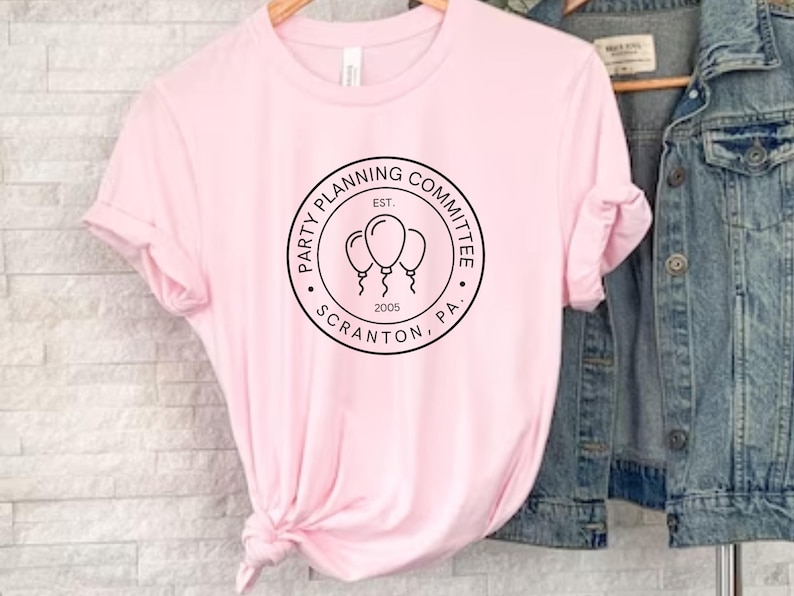 May include: Pink t-shirt with a black and white circle graphic that says "Party Planning Committee, Est. 2005, Scranton, PA" with three balloons inside the circle.